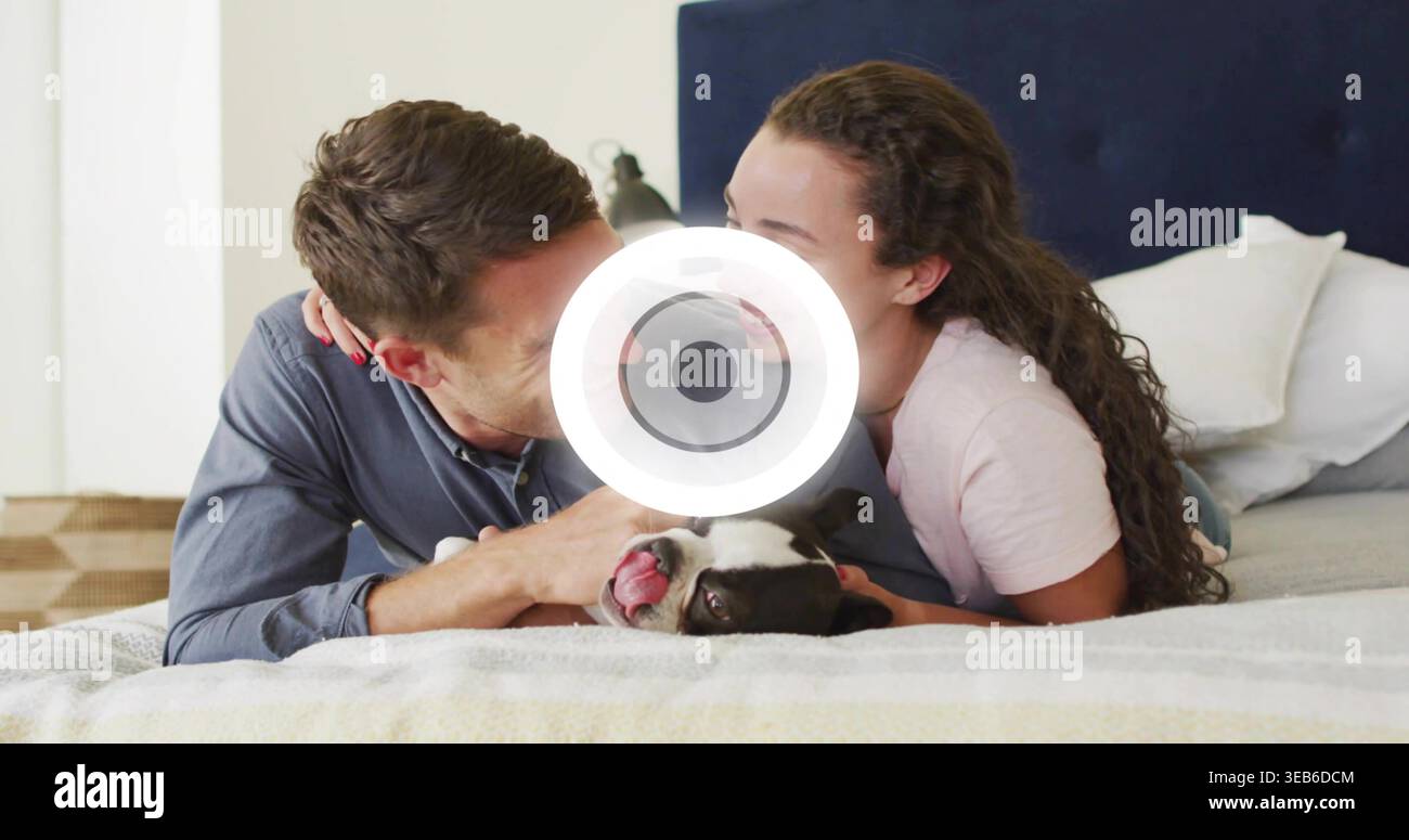 Liegendes Paar, das legere Hemden trägt und sich in Richtung Boston Terrier lehnt, auf dem Bett im Schlafzimmer mit Kissen Stockfoto
