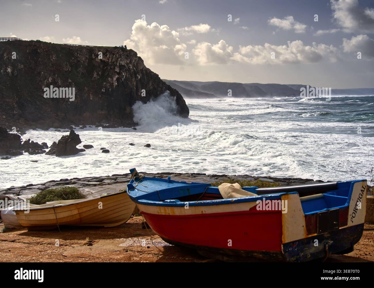 Fischerboote ruhen an einem verwitterten Ufer, während mächtige Wellen gegen die Klippen der portugiesischen atlantikküste krachen und ein raues lan am Meer darstellen Stockfoto