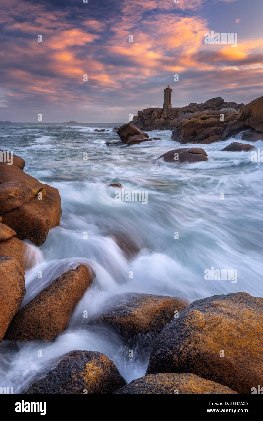 Blick auf den Leuchtturm von Ploumanac'h, der auf rosa Granitfelsen mit stürzenden Wellen unter einem Sonnenuntergang in Perros-Guirec, Bretagne, Frankreich steht. Stockfoto