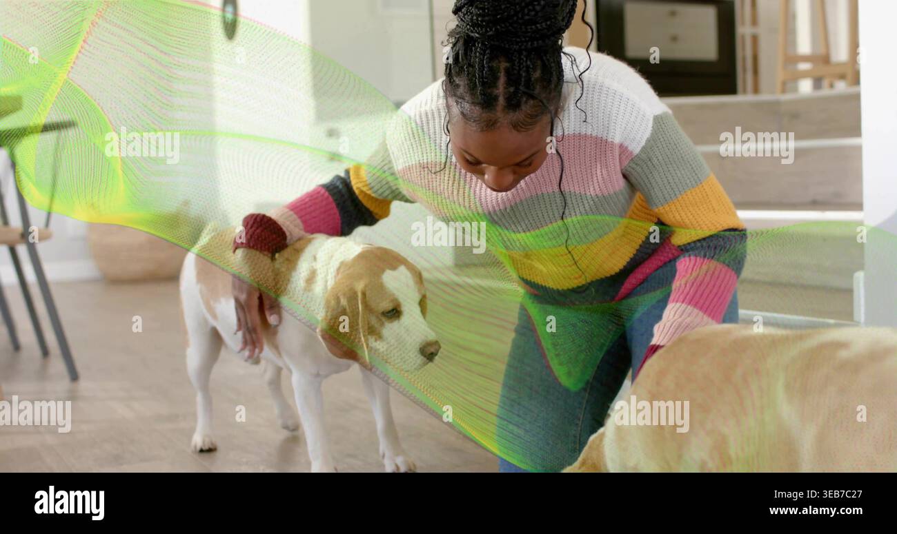 Kniende Frau, die zwei Hunde im Wohnbereich zu Hause streichelt, mit gestreiftem Pullover und Jeans Stockfoto