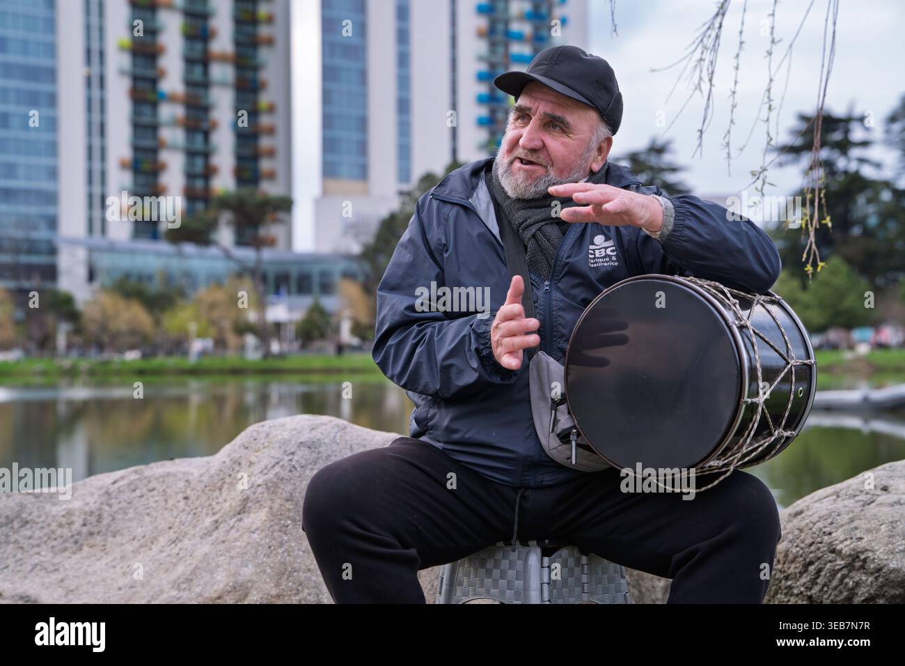 Batumi, georgien 21. april 2026: Ein georgischer Mann spielt eine doli-Trommel und spricht in lässiger Kleidung gegen den Stadtpark Stockfoto