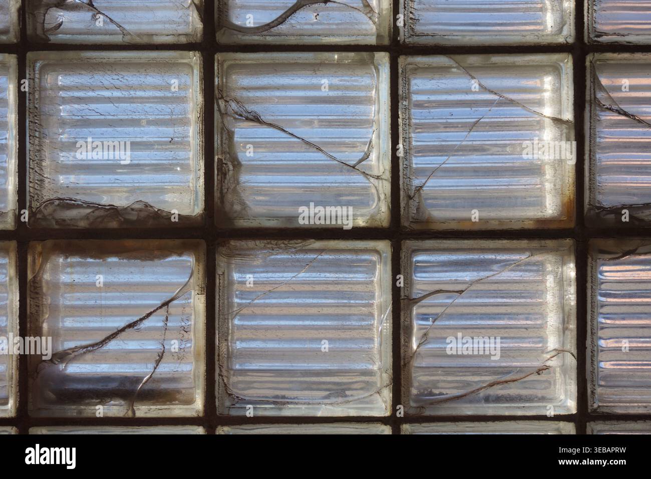 Die Sonne scheint durch ein Fenster aus gerissenen quadratischen Glasblöcken. Stockfoto