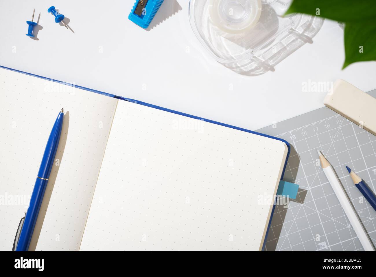 Offenes gepunktetes Notizbuch mit blauem Stift, Bleistiften, Radiergummi, Lineal, Klebeband, Spitzer, Stifte. Workspace-Hintergrund, Copyspace. Stockfoto