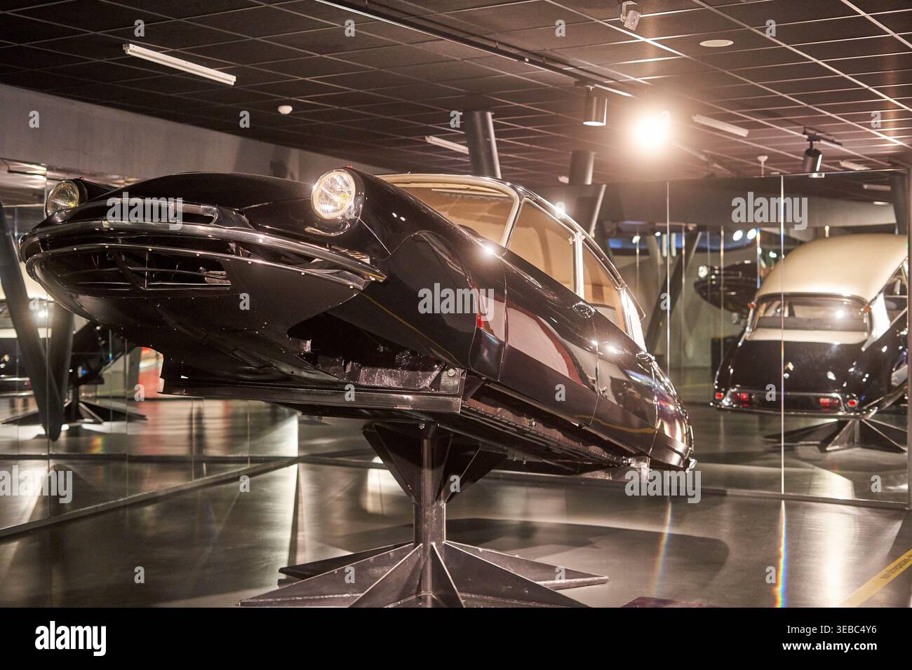 Ein schwarzes Vintage-Luxusauto, wahrscheinlich ein Citroën DS aus den 1950er-1960er Jahren, auf einem schrägen Podest in einem modernen Automuseum ausgestellt. Das Fahrzeug ist Stockfoto