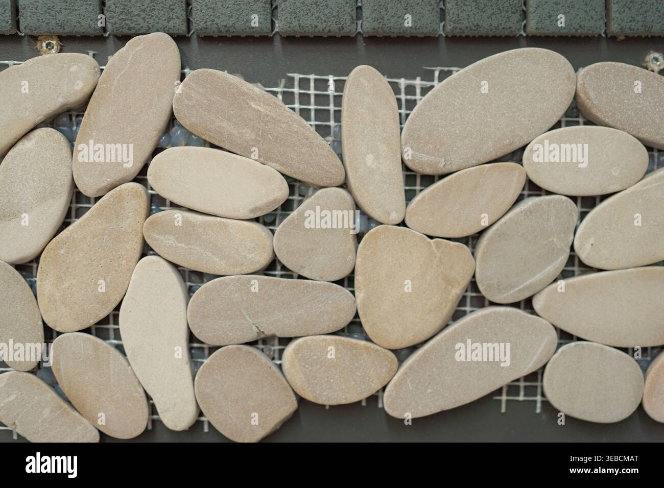 Nahaufnahme von glatten, ovalen Kieselsteinen, die auf Gitter angeordnet sind. Weiche Naturtöne und abgerundete Formen schaffen eine ruhige organische Textur für Badezimmer, Spa oder Stockfoto