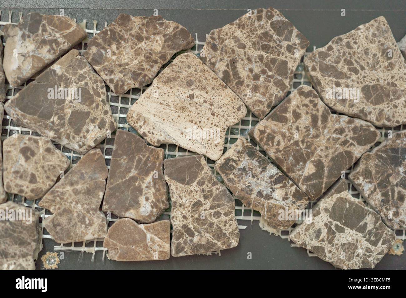Nahaufnahme unregelmäßiger brauner Steinmosaikfliesen auf Netzrücken. Natürliche Textur mit organischen Formen und Erdtönen, ideal für Bodenbeläge Stockfoto