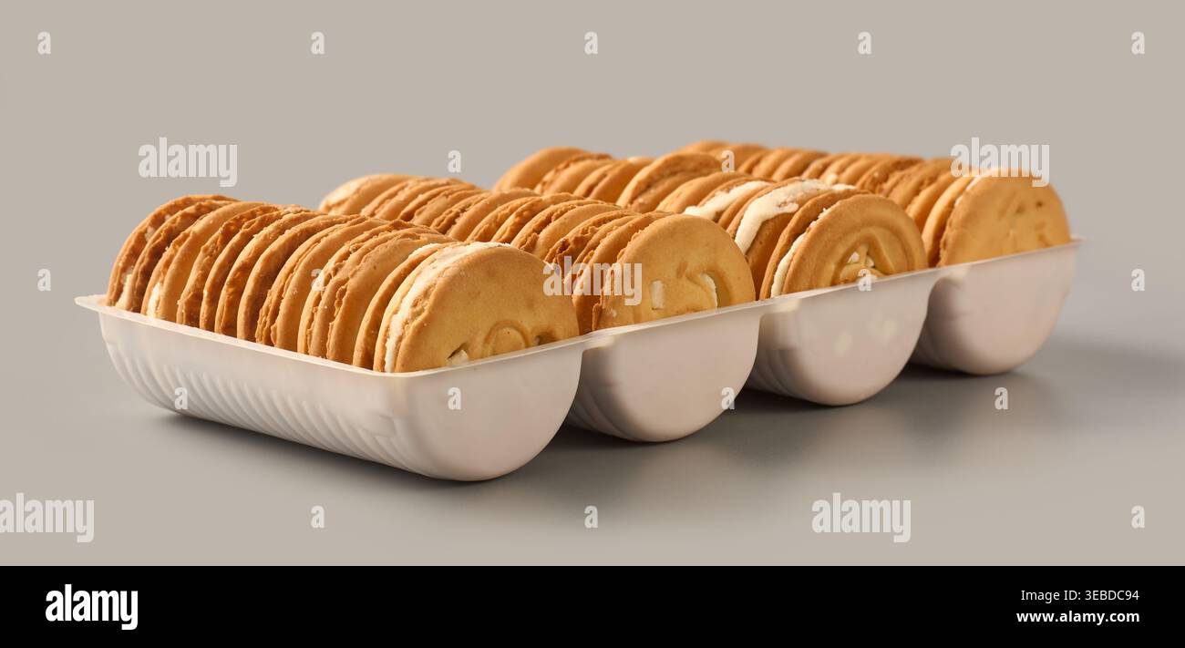 Cremefarbene Sandwichkekse in weißer Kunststoffschale isolierter grauer Hintergrund, runde Kekse mit strukturierter Oberfläche, Seitenansicht des Concept für Süßwaren Stockfoto