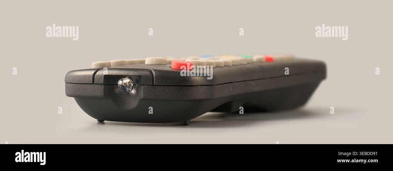 Schwarze Kunststoff-Fernbedienung mit Infrarot-Senderlampe auf grauem Hintergrund, drahtlose Technologie und Signalübertragung, Seitenansicht mit Weichfokus Stockfoto