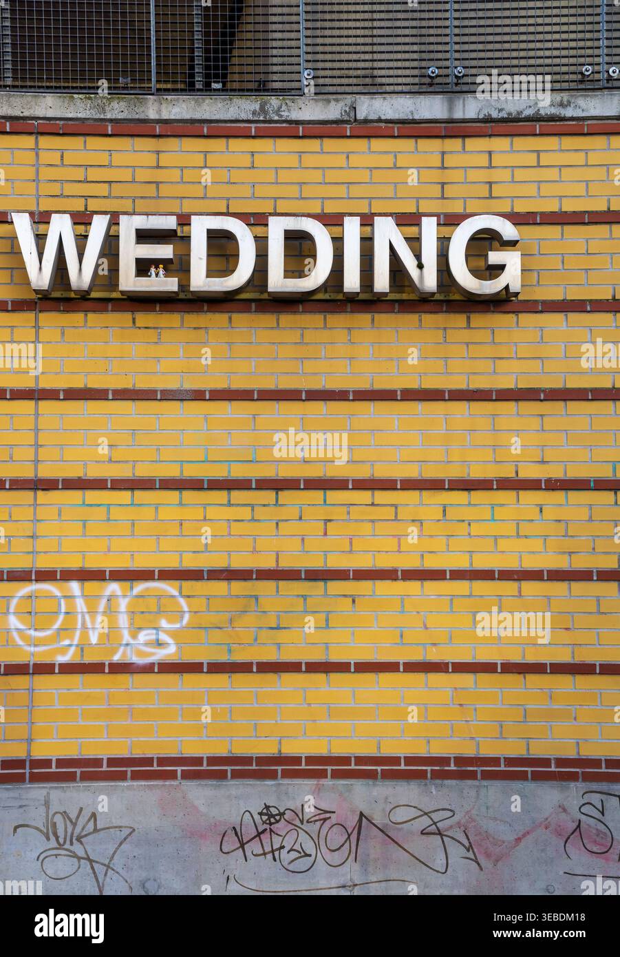 Vertikale Ansicht des Bahnhofsschilds „Wedding“, das an einer gelben Ziegelwand am S-Bahnhof Wedding in Berlin angebracht ist. Stockfoto