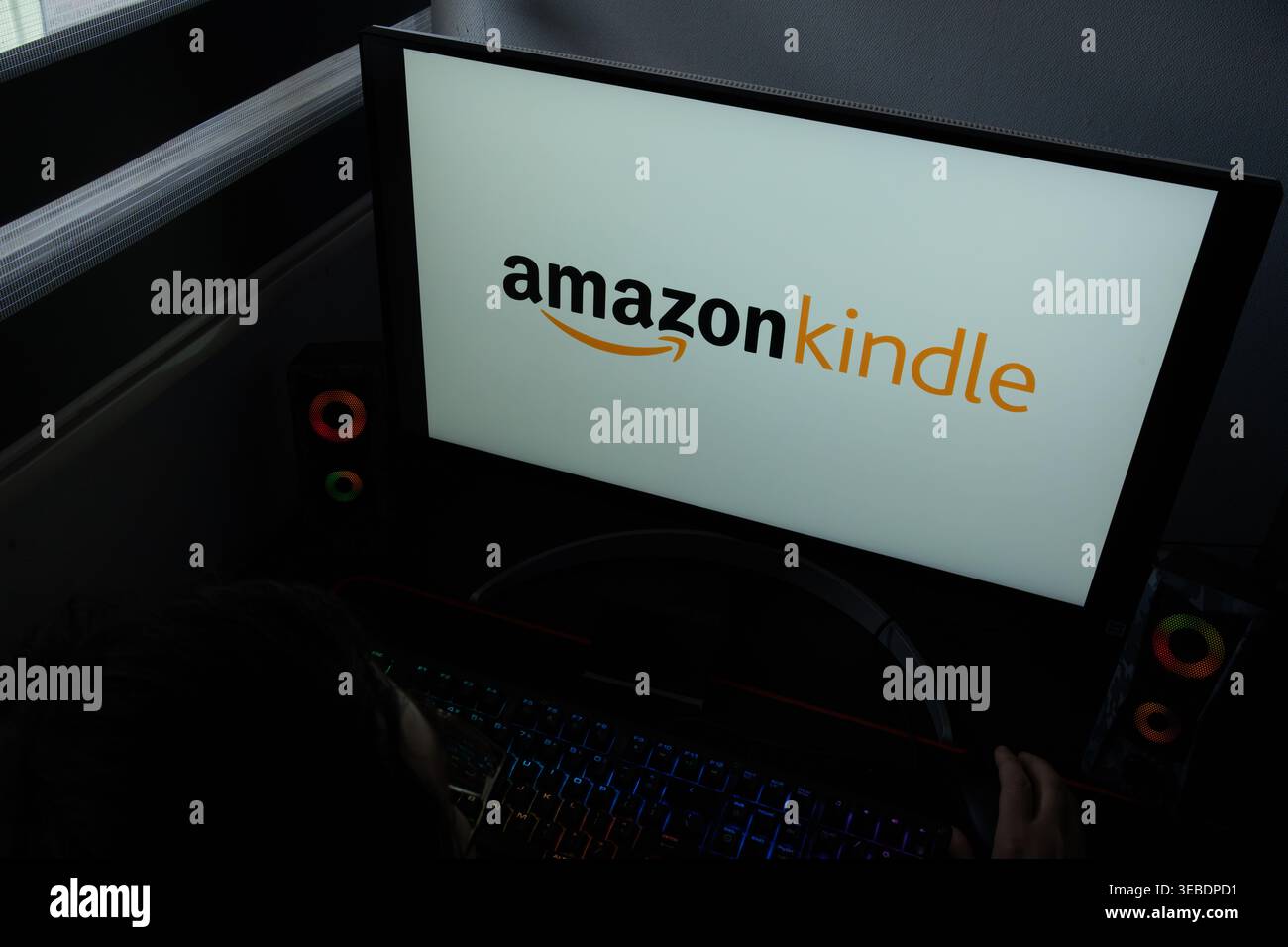 Das Amazon Kindle Logo wird auf einem Computermonitor in einem schwach beleuchteten Heimbüro angezeigt Stockfoto