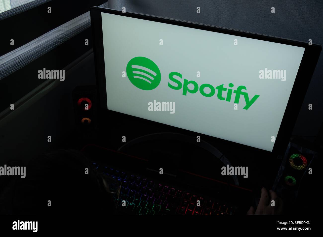Das Logo und die Wortmarke des Spotify Music Streaming Service werden auf einem Computermonitor in einem dunklen Heimbüro angezeigt Stockfoto