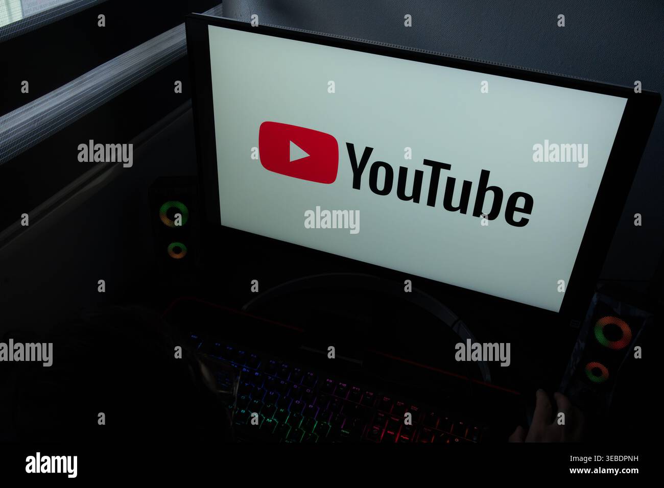 Das Logo und die Wortmarke der YouTube-Plattform werden auf einem Computermonitor in einem dunklen Raum angezeigt Stockfoto