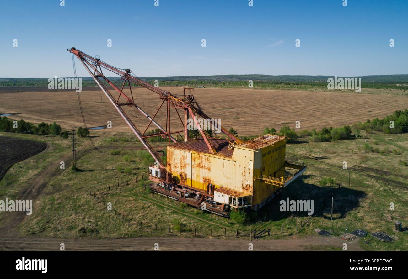 Der massive industrielle Schleppbagger ruht auf einem offenen Feld, umgeben von karger Vegetation und unbefestigten Straßen Stockfoto