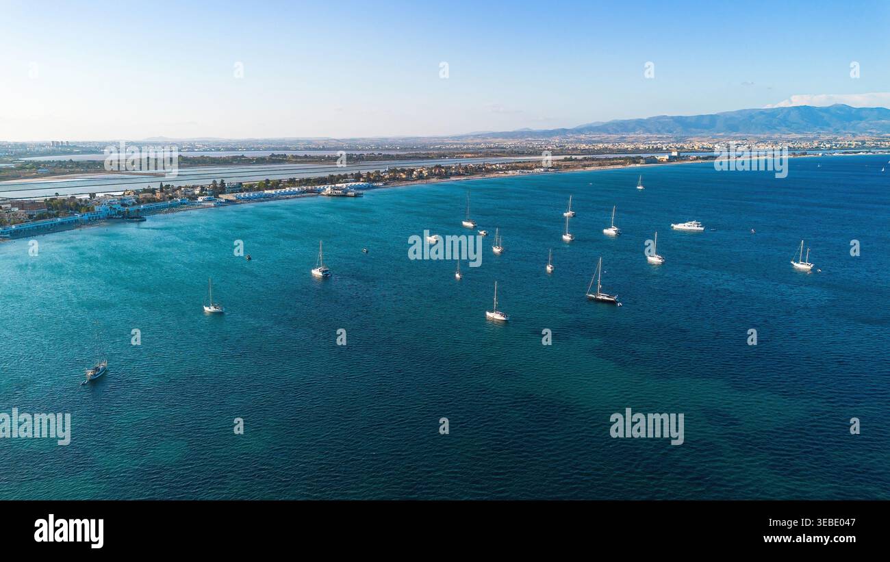 Aus der Vogelperspektive auf Segelboote vor Anker im türkisfarbenen Wasser des Poetto Strandes mit Salinen und Bergen im Hintergrund, Cagliari, Sardinien, Italien Stockfoto