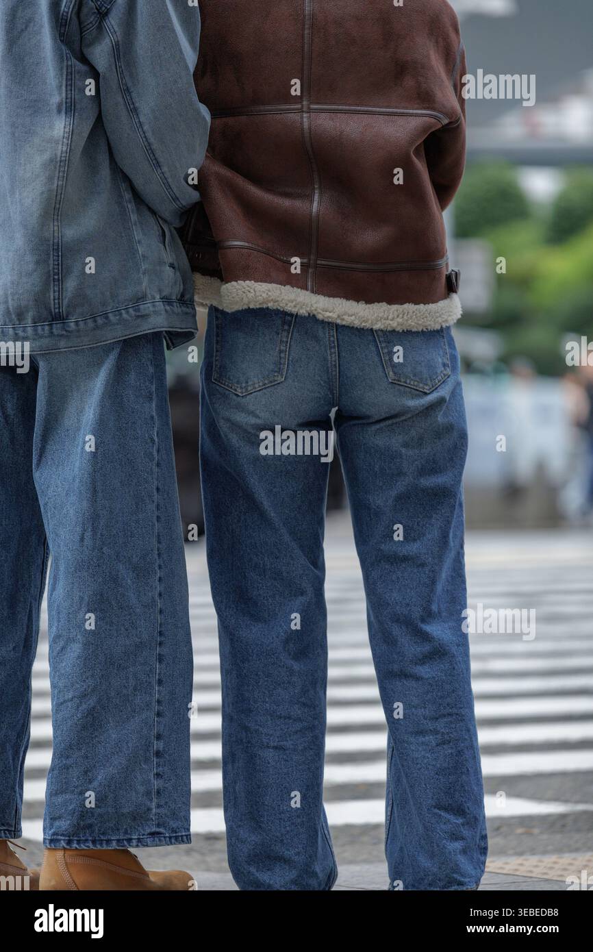 Jacke aus Denim und Leder mit warmem Lammfellbesatz, das Paar steht an einem Quersteg, während der eine den Arm des anderen sanft hält, in subtiler Geste der Verbindung. Stockfoto