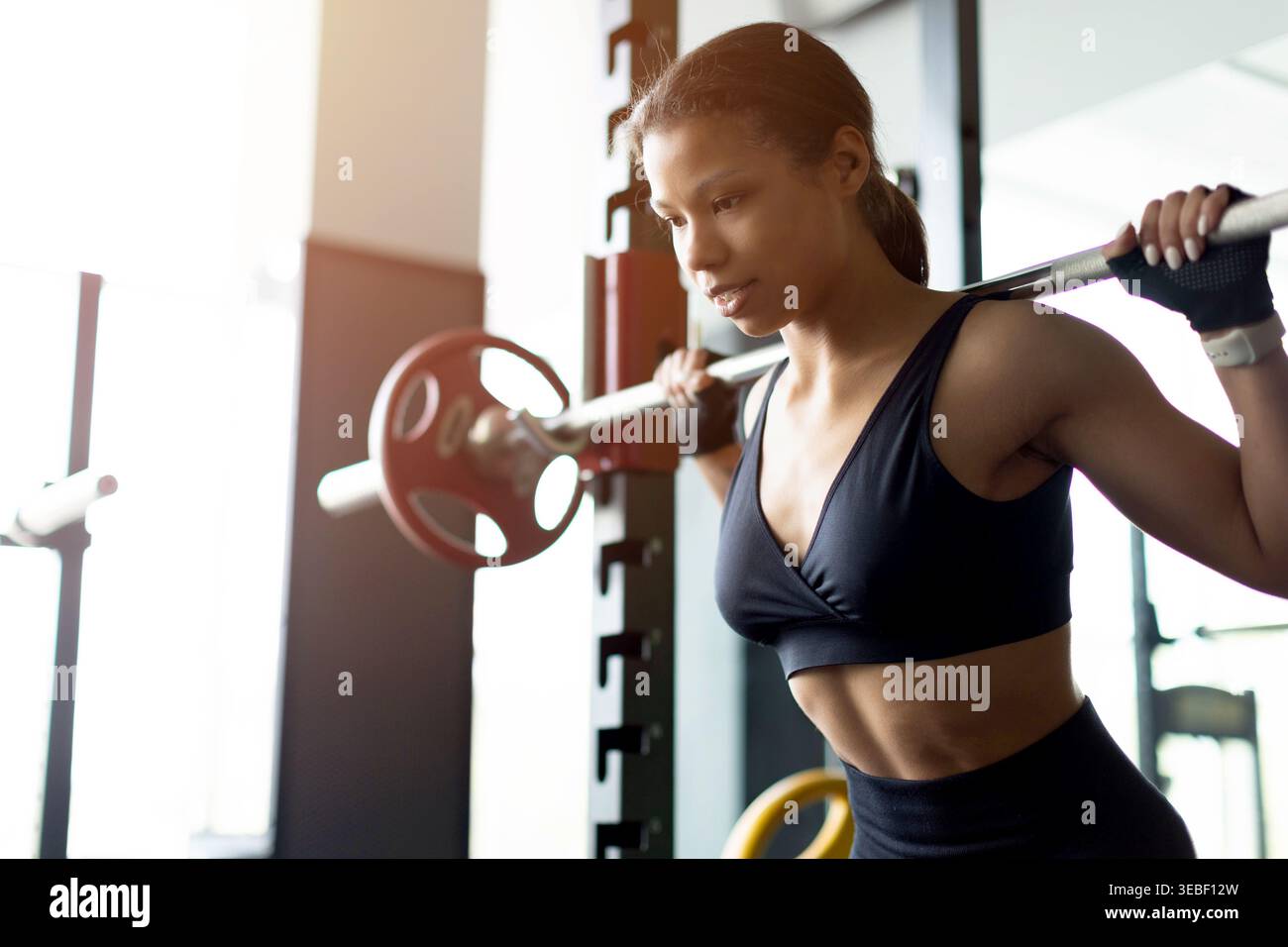 Junge Schwarze Frau, die Langhantel auf Hockgestell im Fitnessstudio packt Stockfoto