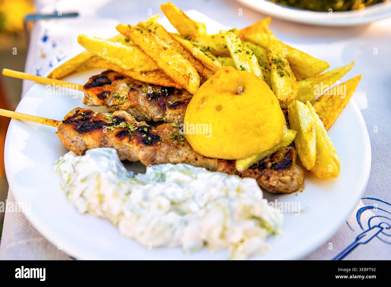 Hühnchenspieß, Tzatziki-Joghurt-Gurkensauce, Pommes Frites auf weißem Teller im traditionellen griechischen Restaurant auf Ikaria, Griechenland Stockfoto