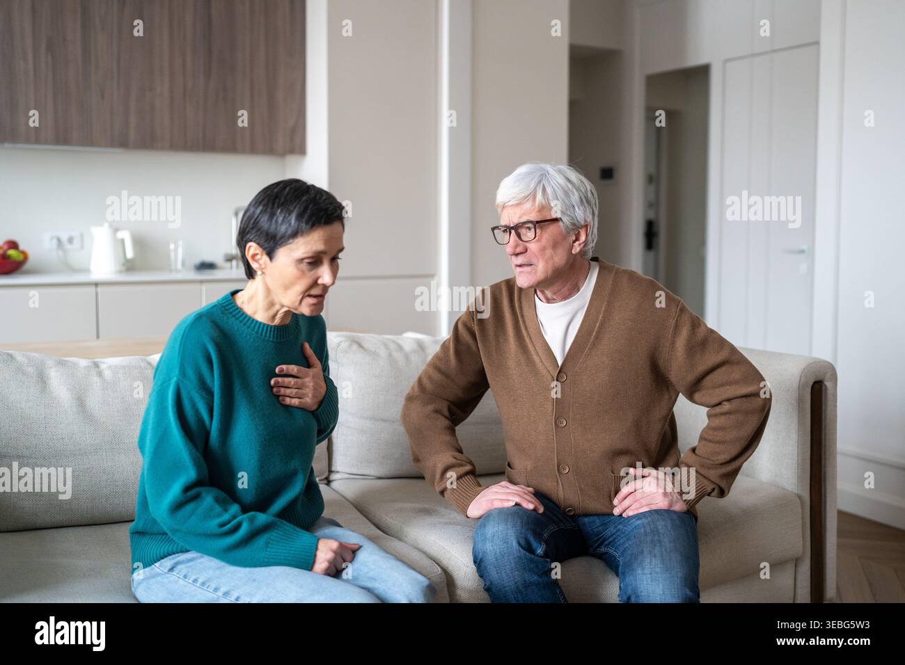 Ältere Frau, die plötzliche Herzschmerzen empfindet, während der ältere Ehemann Sorge und Unterstützung zeigt. Stockfoto