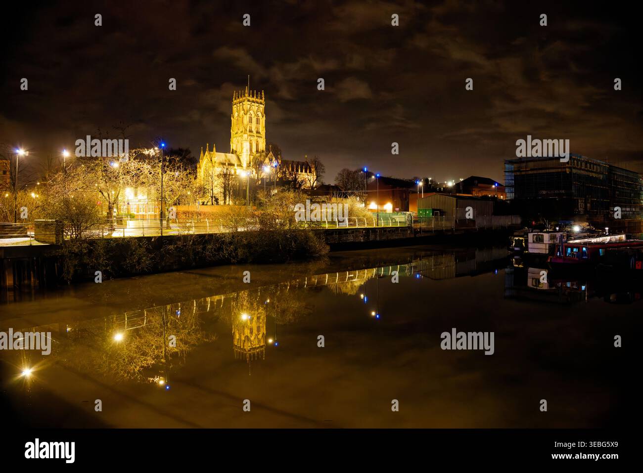 Ein beleuchtetes Doncaster Minster spiegelt sich nachts im dunklen Wasser eines Kanals im Stadtzentrum von Doncaster, South Yorkshire, wider. Stockfoto