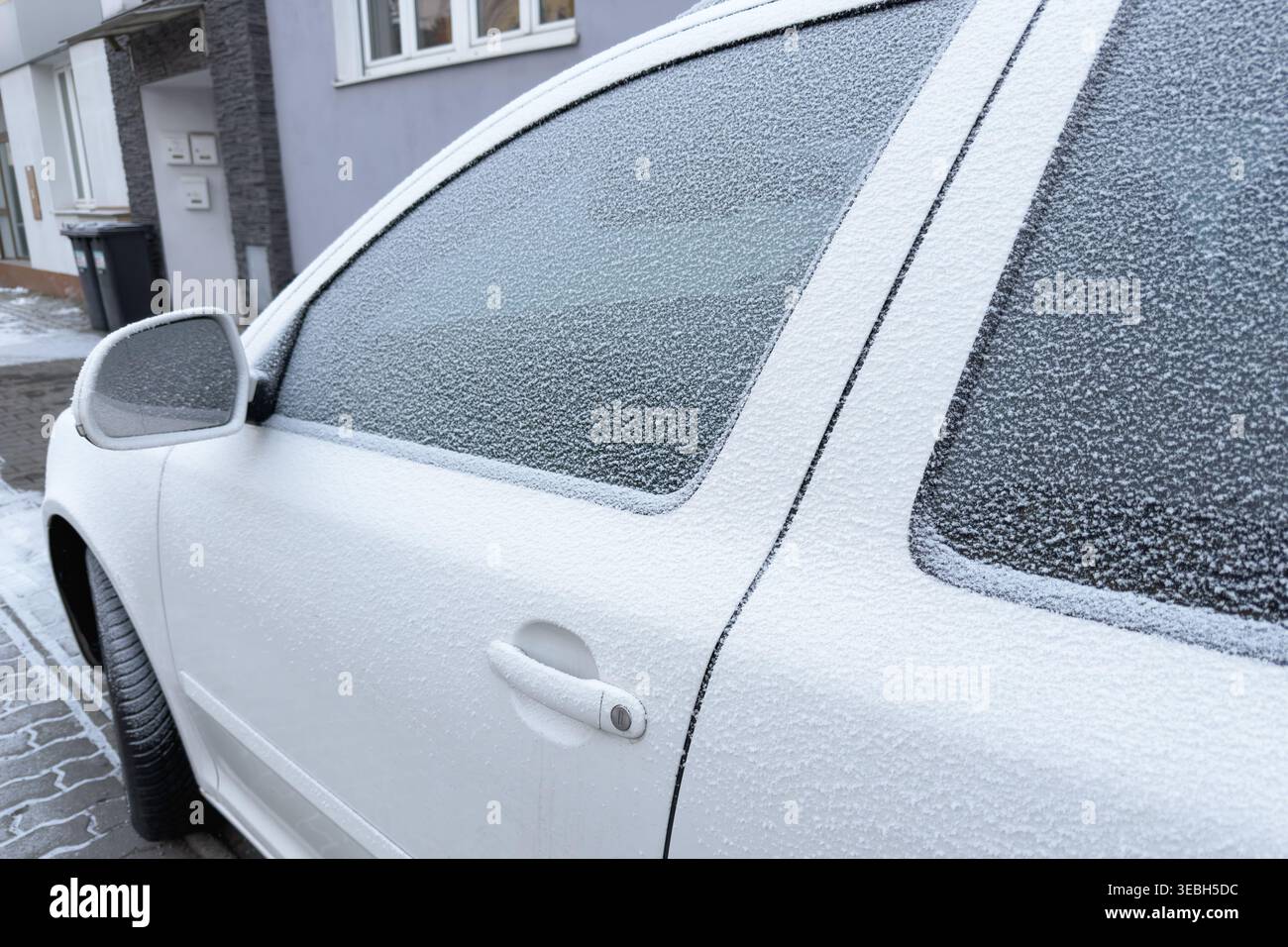Die eisige Berührung des Winters bedeckt ein Auto, dessen Fenster in einem zarten Frost verborgen sind. Die Welt draußen verschwimmt hinter einem kristallklaren Vorhang von kalter Schönheit. Stockfoto