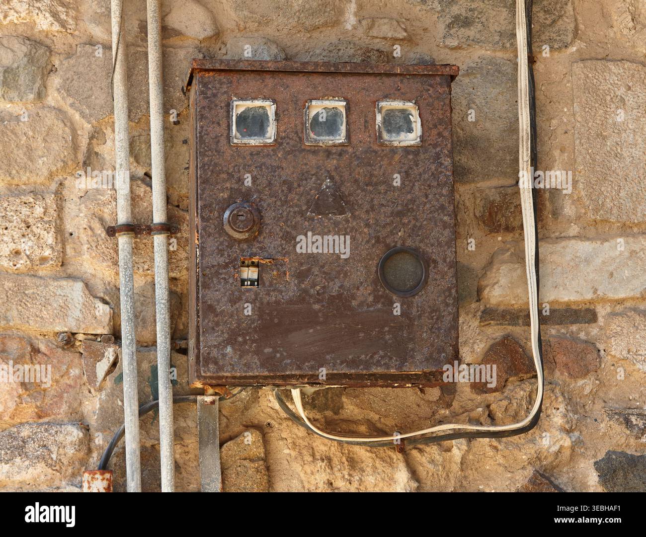 Rostige elektrische Schalttafel, die an einer Steinmauer befestigt ist, mit sichtbarer Verkabelung und verwittertem Aussehen, die industrielle und historische Saibling hervorhebt Stockfoto