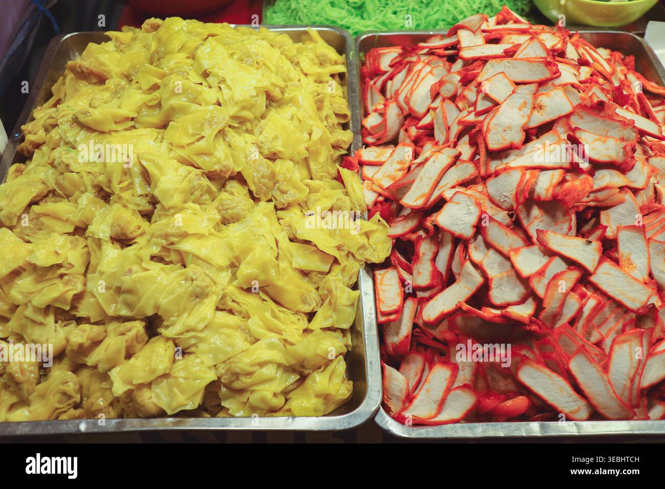 Tabletts mit Wonton und rot geröstetem Schweinefleisch von oben, die echte Street Food-Zutaten im thailändischen Nudelgeschäft zeigen. Stockfoto