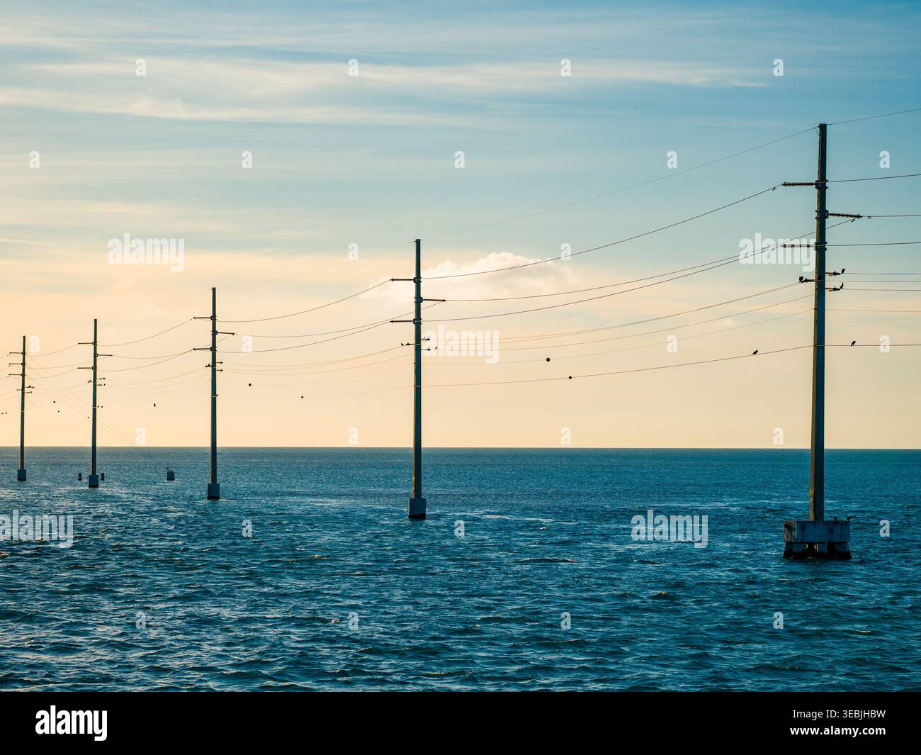 Die elektrischen Betonmasten erstrecken sich über das offene Meer in Richtung Horizont unter einem weichen Sonnenuntergangshimmel entlang des Overseas Highway in den Florida Keys, USA. Stockfoto