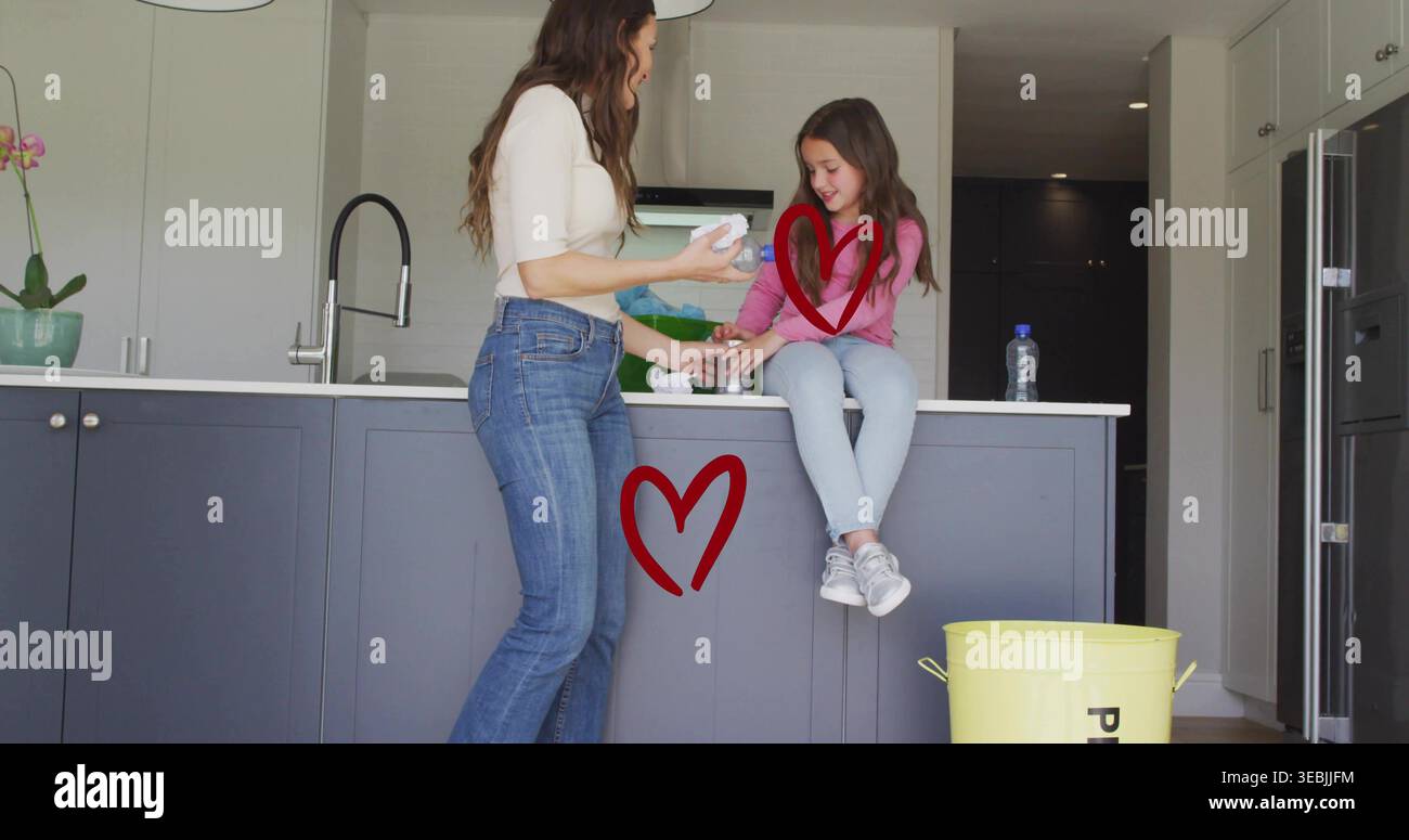 Frau mit cremefarbenem Oberteil, Jeans, die ein Mädchen auf der Kücheninsel mit weißem Tuch überreicht, mit gelbem Eimer Stockfoto