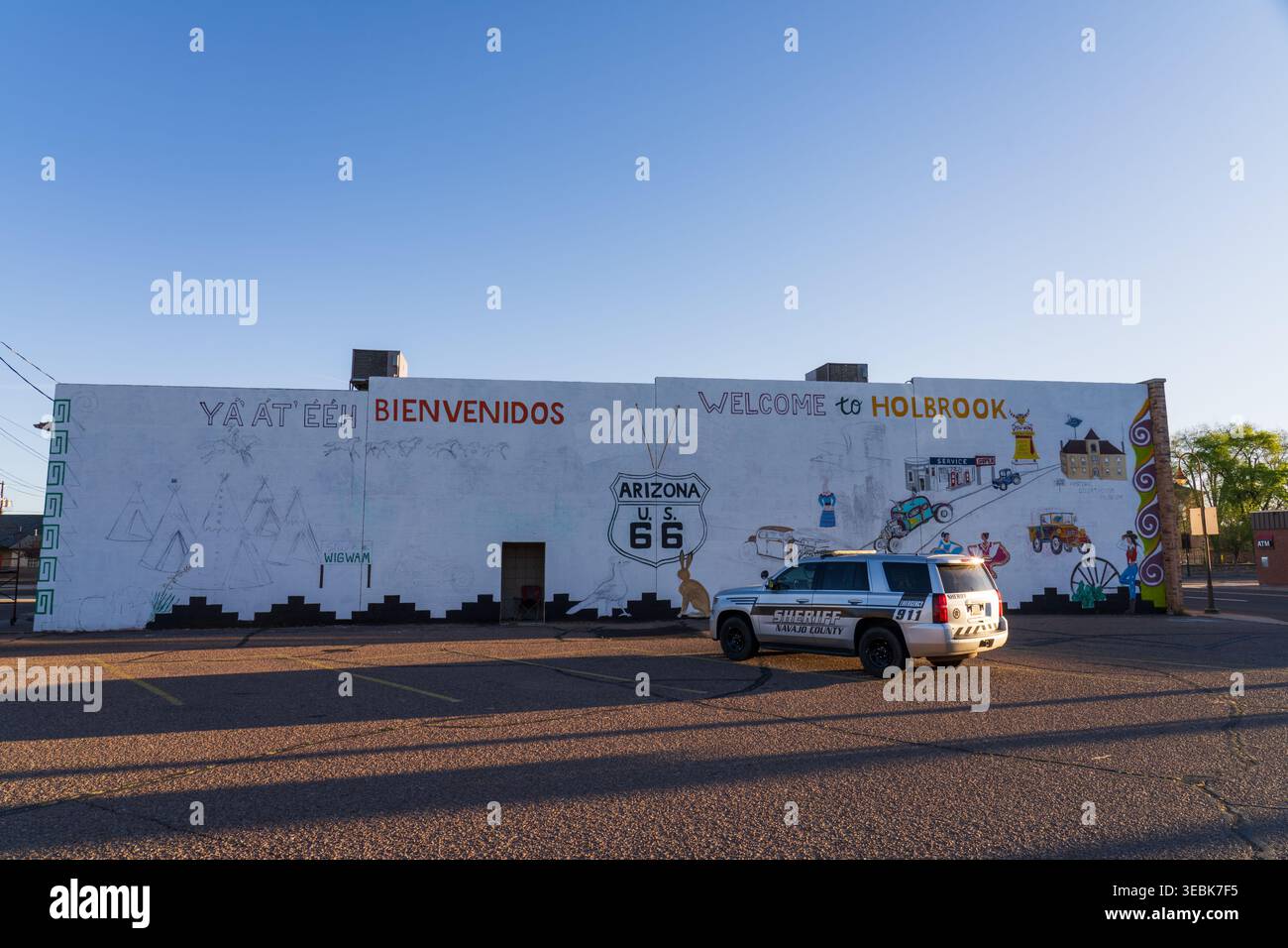 Sheriff-Patrouillenfahrzeug, das neben einem farbenfrohen Willkommensschild für Holbrook, Arizona, geparkt ist, das ein historisches Schild der Route 66 unter einem strahlend blauen Himmel zeigt Stockfoto