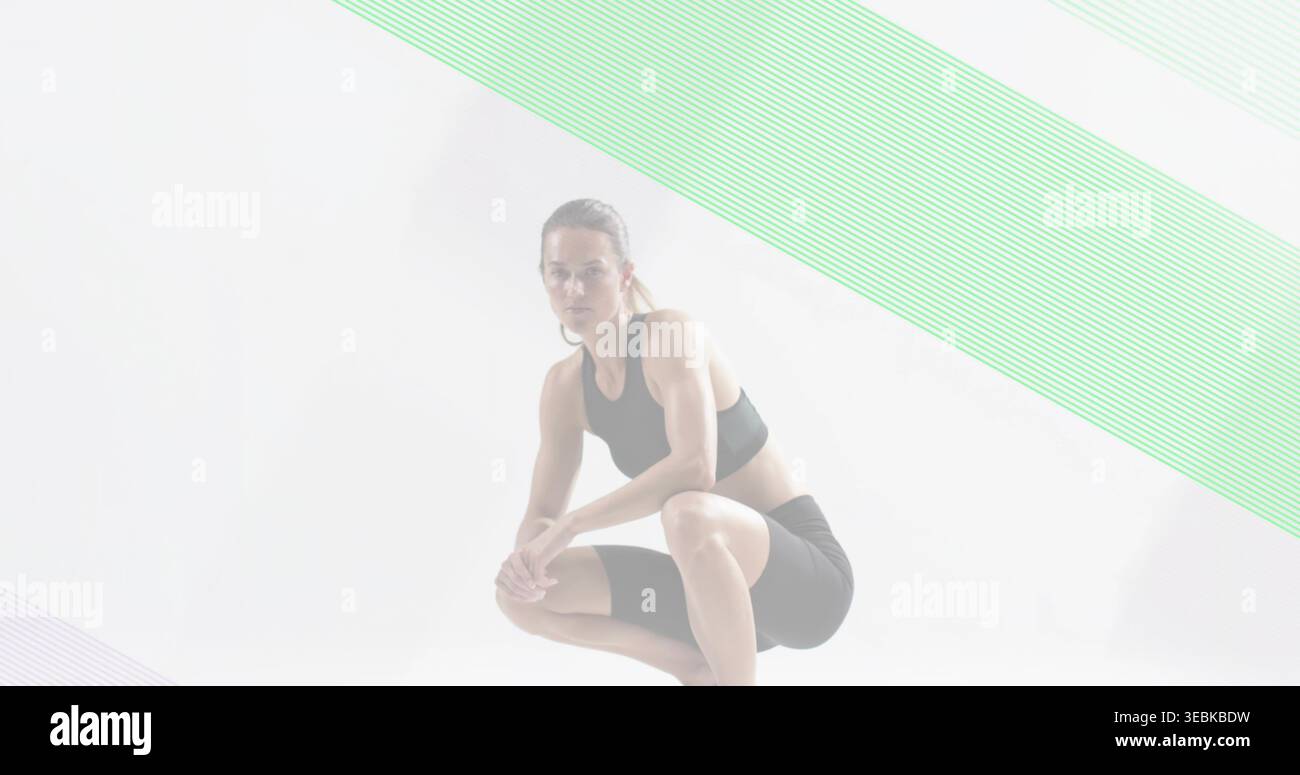 Posierender Athlet in niedriger Hocke im Studio, mit schwarzem Sport-BH, Shorts, Basketball, Mint-Lavendel-Bands Stockfoto