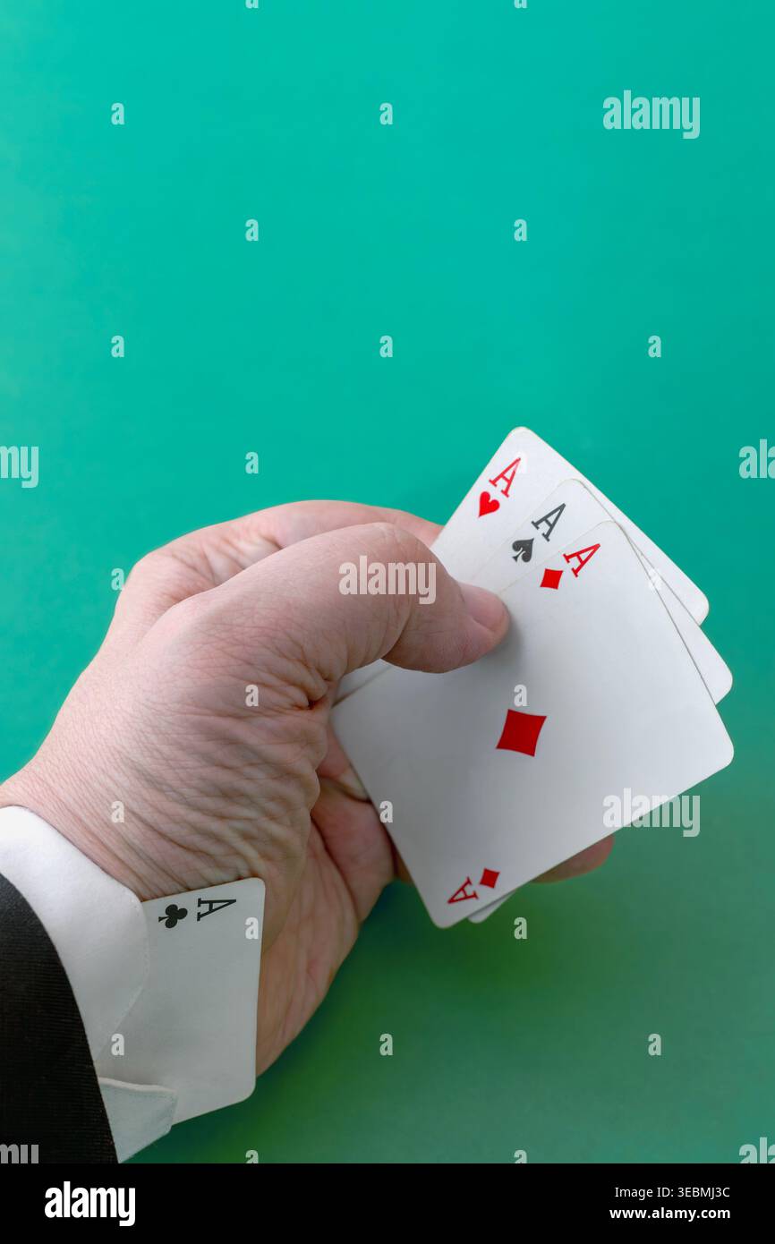 Männliche Hand im Anzug mit drei Assen, das vierte Ass versteckt im Ärmel auf grünem Hintergrund. Stockfoto