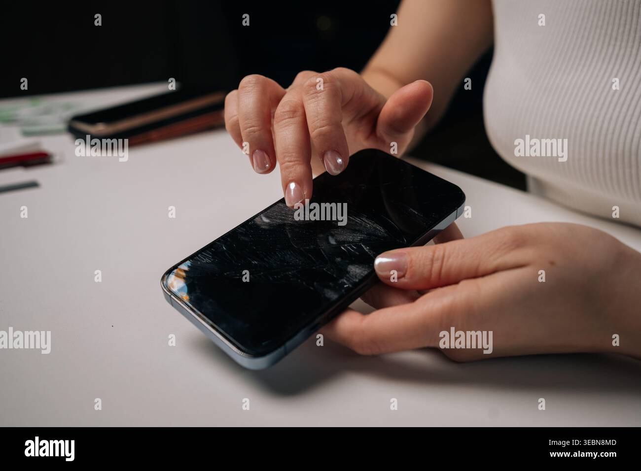 Frau zieht beschädigte Displayschutzfolie vom Smartphone ab, legt rissige Schutzfolie auf weißer Oberfläche frei, wodurch ein beeinträchtigter Zustand des Geräts sichtbar wird. Stockfoto