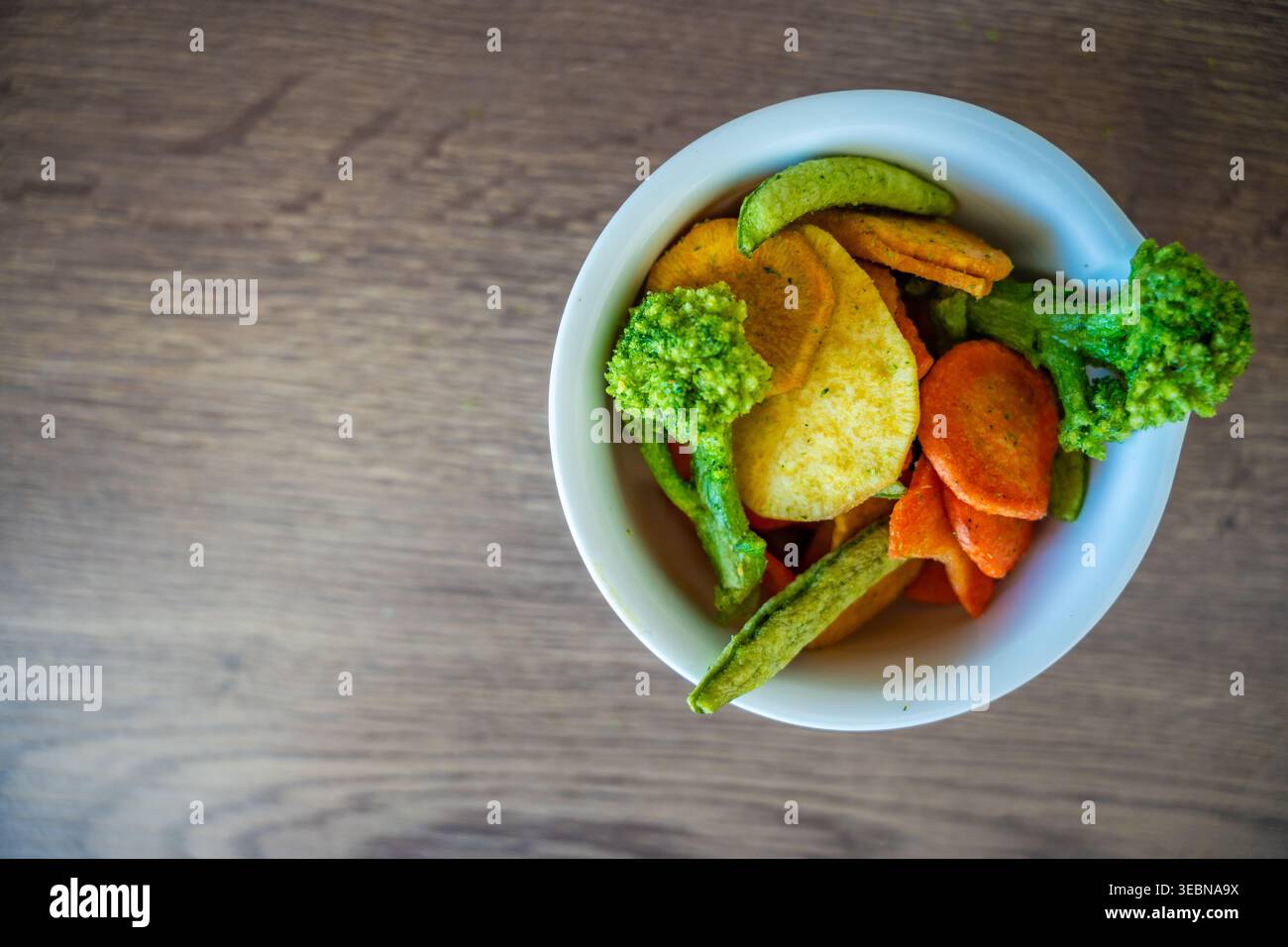 Gemischte Gemüsechips in Schüssel mit Kopierraum auf hölzernem Hintergrund. Gesunder Snack und Clean Eating Konzept ohne Salz Zucker oder Zusatzstoffe. Stockfoto