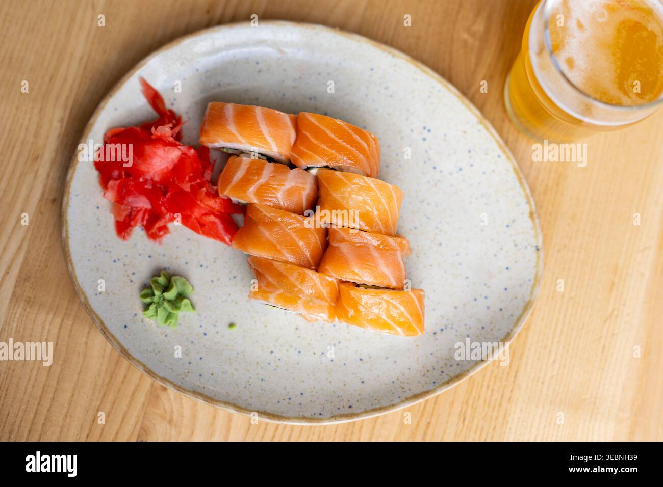 Lachs-Sushi-Rolls Mit Bier. Blick von oben auf Lachs-Sushi-Brötchen mit eingelegtem Ingwer, Wasabi und Bier auf einem hölzernen Restauranttisch. Stockfoto