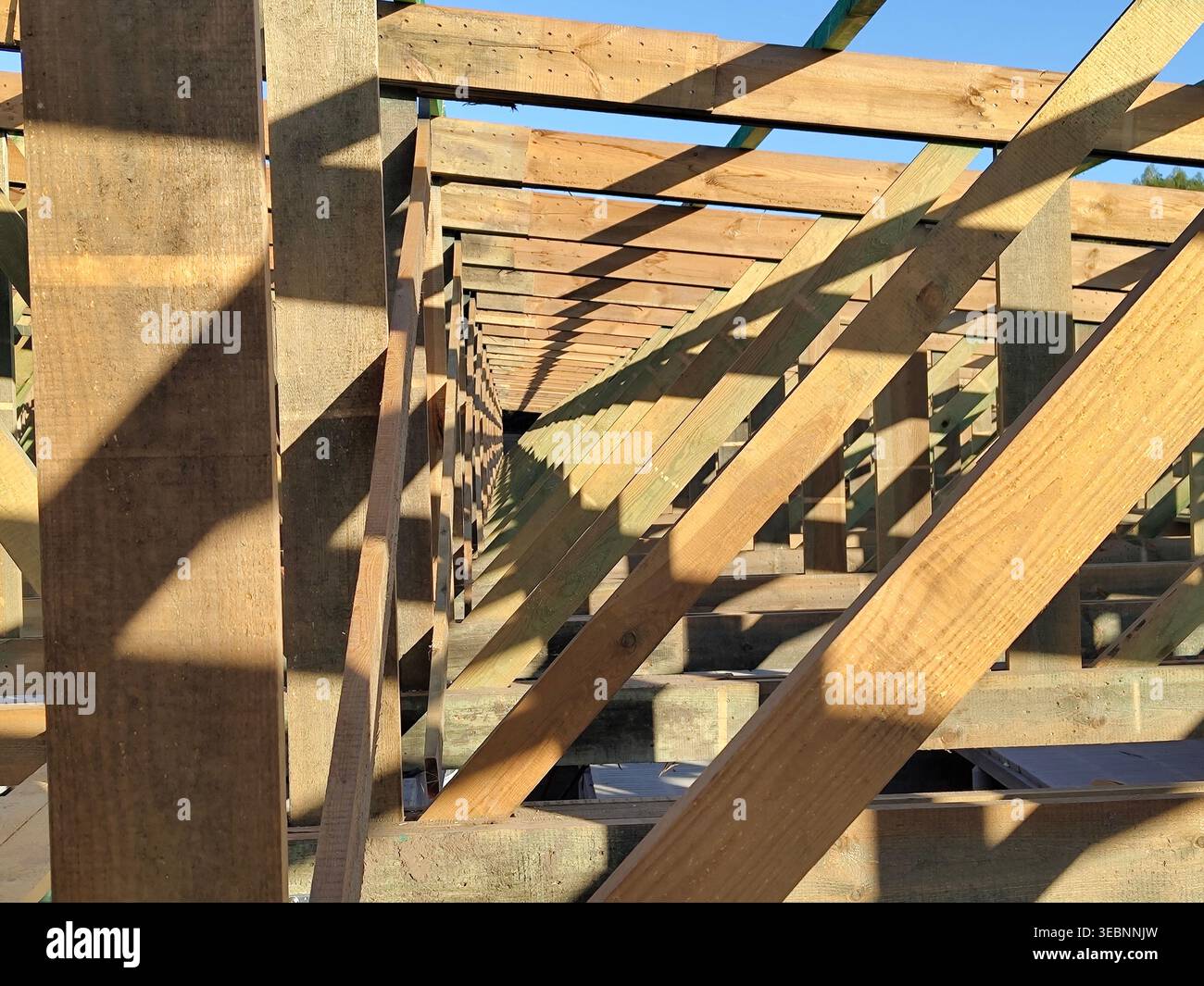 Holzdachrahmenkonstruktion im Bau mit Balken, Sparren und Stützen, die bei Sonnenlicht auf der Baustelle geometrisches Muster bilden. Konstruktion, c Stockfoto