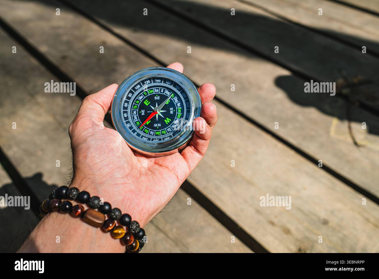 Hand mit Armband, das magnetischen Kompass über rustikalem Holztisch hält, Bergwald im Freien wandern Stockfoto