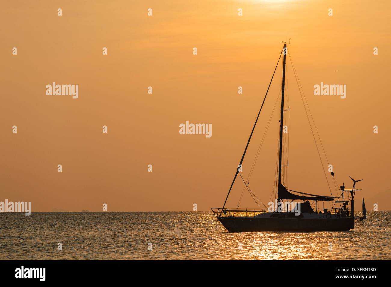 Silhouette einer Segelyacht auf ruhigem Meer bei goldenem Sonnenuntergang, friedliche abendliche Meereslandschaft mit warmer Lichtreflexion auf dem Wasser Stockfoto