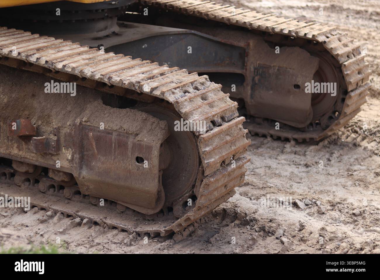 Baggerketten auf Sand aus nächster Nähe. Detaillierte Ansicht der leistungsstarken Metallspuren von Baumaschinen, die beim Arbeiten auf sandigem Boden mit Schlamm bedeckt sind Stockfoto