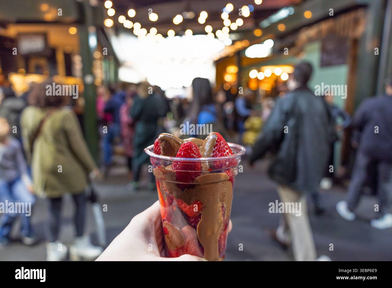 Hand in der Hand mit Schokolade überzogenen Erdbeeren auf einem geschäftigen Straßenmarkt Stockfoto