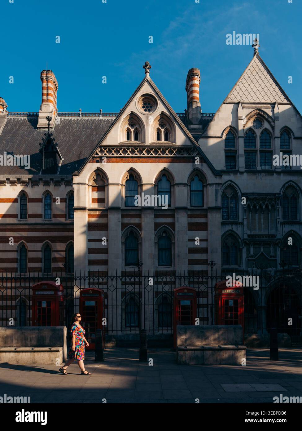 Der Blick auf die königlichen Gerichte steht hoch vor dem azurblauen Himmel und ihre kunstvolle gotische Architektur wirft lange Schatten auf den Bürgersteig, wo ein Wo Stockfoto
