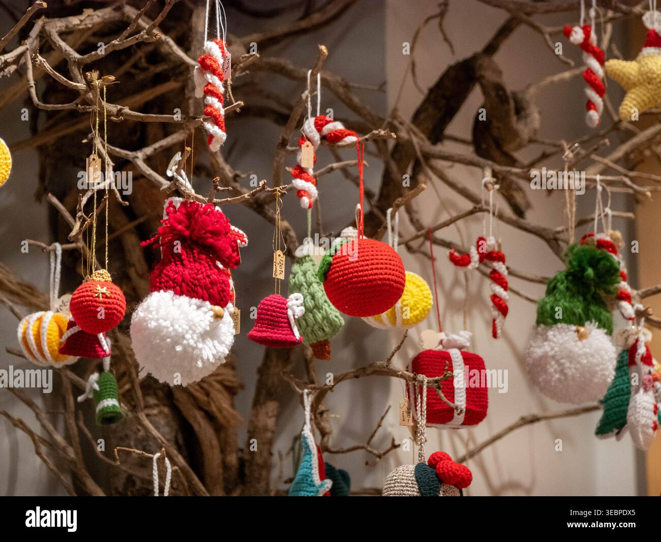 Bezaubernde Sammlung handgemachter Weihnachtsschmuck in leuchtendem Rot und weiß, die von rustikalen Holzzweigen in einer festlichen Präsentation aufgehängt werden Stockfoto