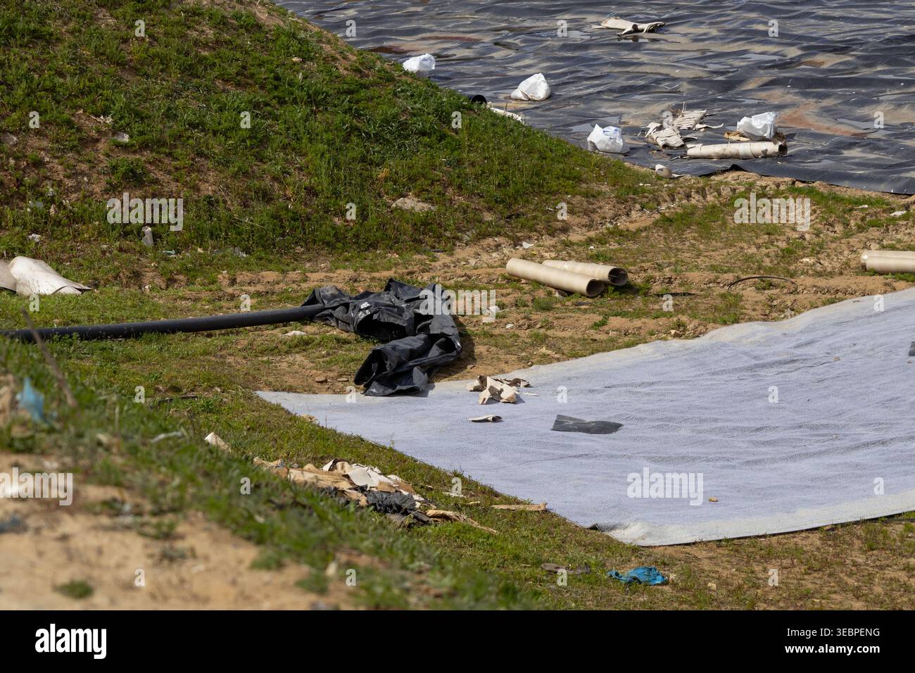 Müll ist auf dem Boden auf der Deponie verstreut, wobei einige Bereiche mit Kunststoffplatten bedeckt sind. Müllsäcke und Abfallmaterialien sind in der Nähe des e sichtbar Stockfoto
