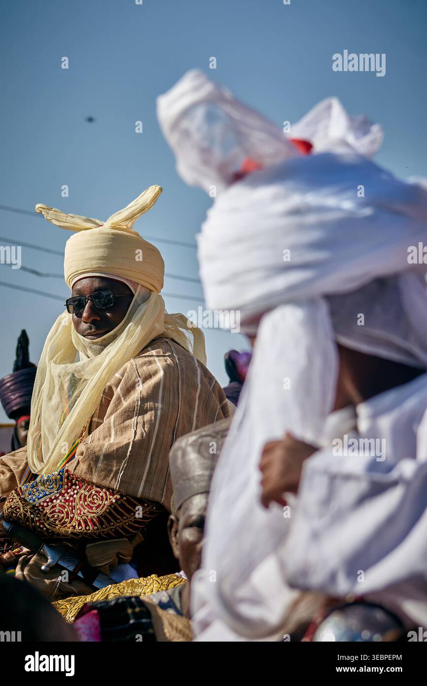 Zaria City, Nigeria - 22. März 2026: Blick auf eine königliche Figur in warmer Creme, traditioneller Kleidung und dunkler Sonnenbrille, ein markanter Kontrast zur Brig Stockfoto