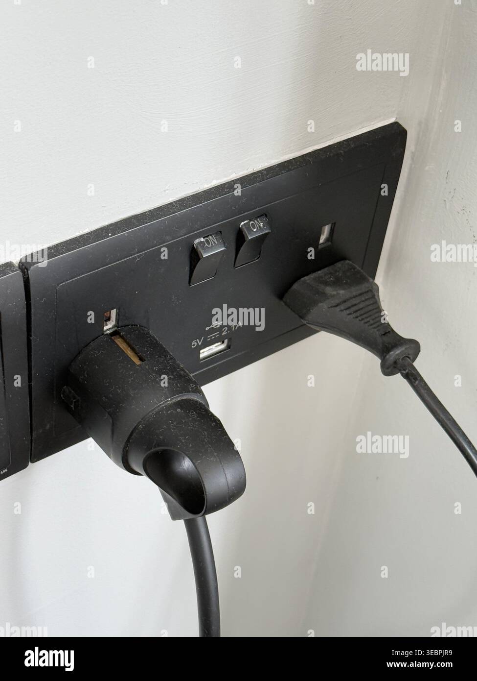 Steckdose mit zwei eingesteckten Kabeln an einer weißen Wand, Nahaufnahme. Mobiles Foto Stockfoto
