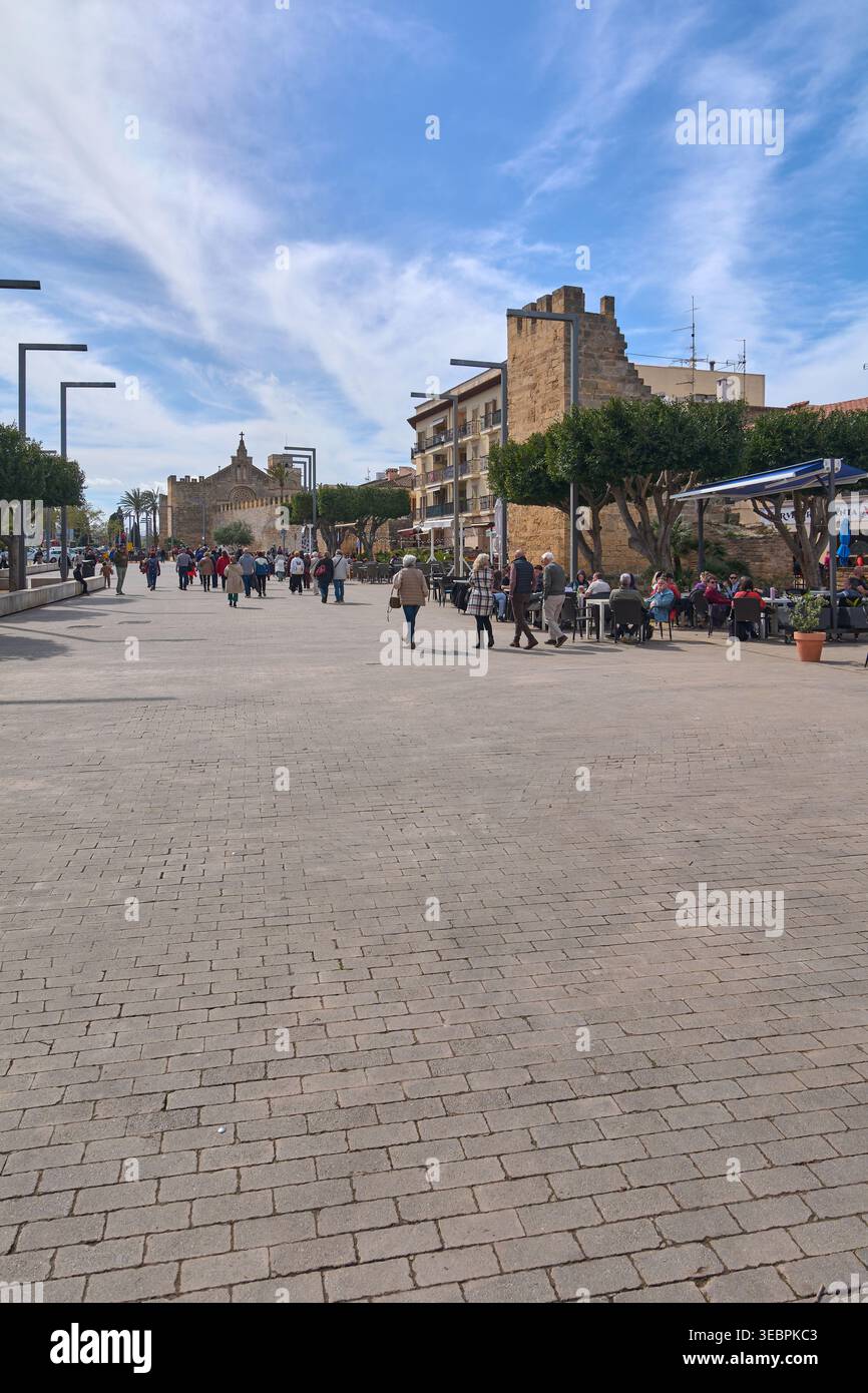 Mallorca Spanien - 27. April 2026: Touristen schlendern durch den weitläufigen steinplatz in Alcudia neben den historischen mittelalterlichen Mauern und der Kirche Sant Jaume Stockfoto
