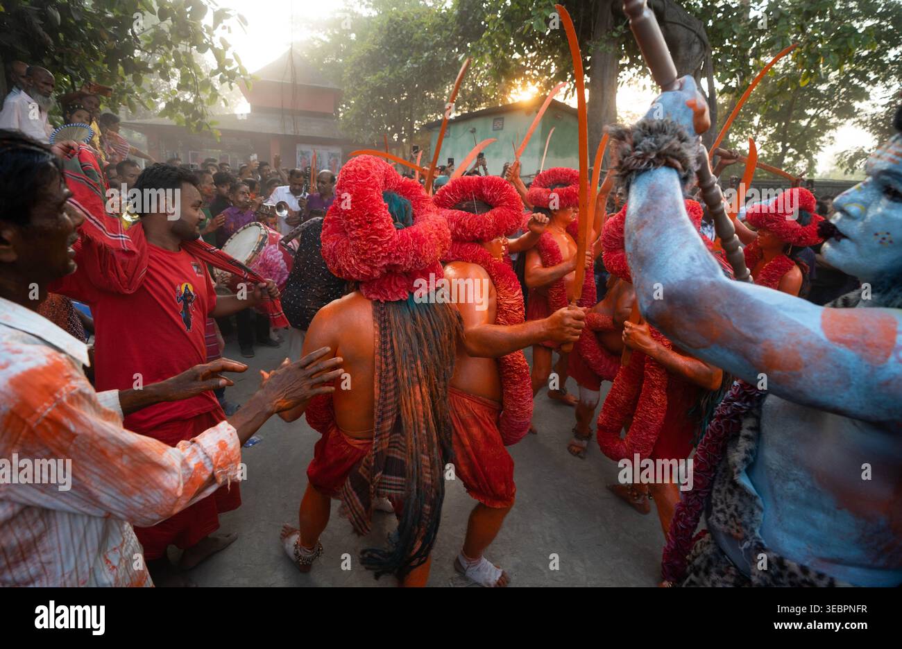 Munshiganj, Bangladesch - 13. April 2025: Ein Blick auf lebendige Künstler in markanter oranger Körperfarbe und raffinierten roten floralen Kopfschmuck Stockfoto