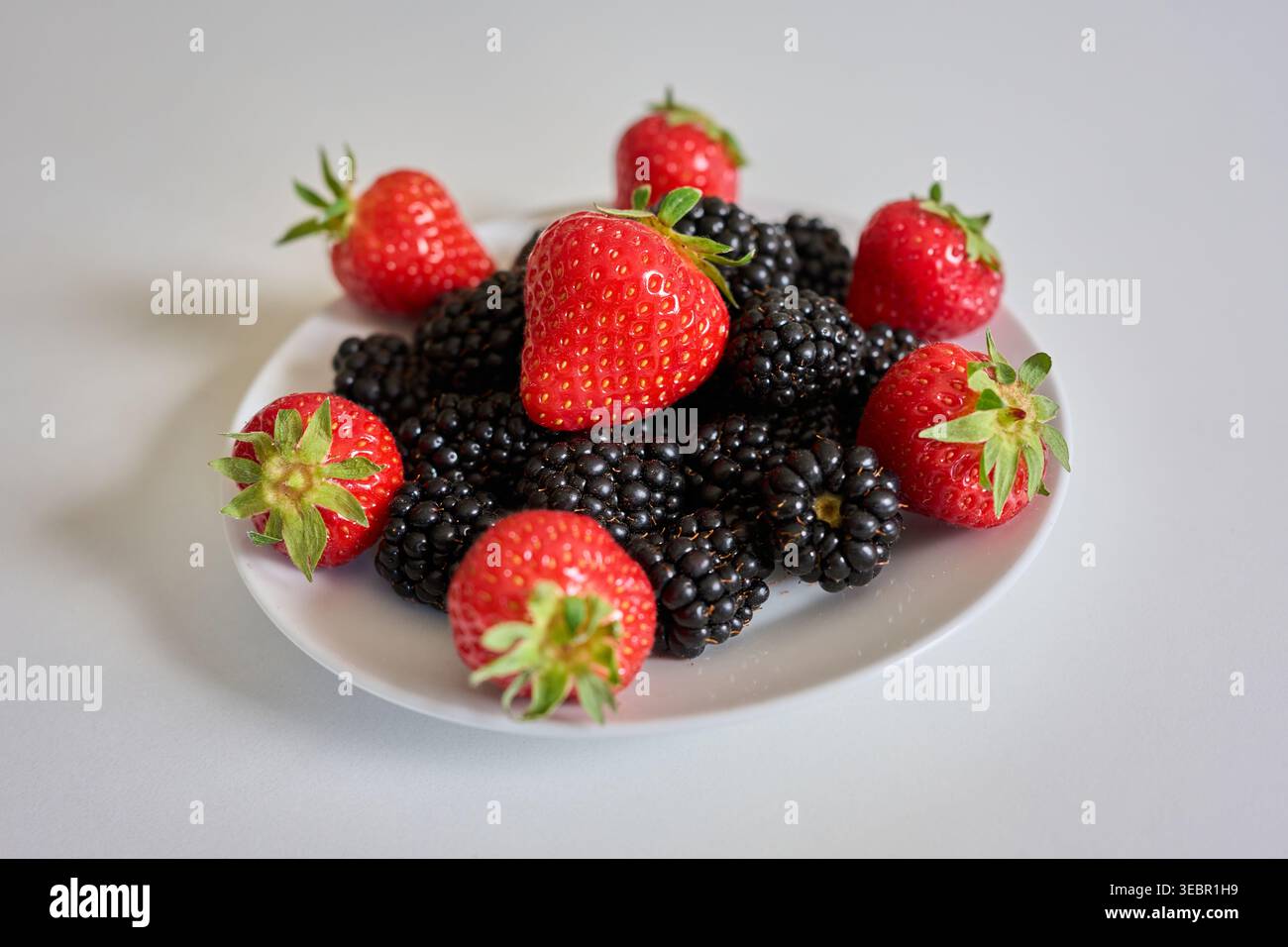 Frische reife Erdbeeren und Brombeeren auf einem weißen Teller auf weißem Hintergrund. Gesunde Mischbeeren für die Sommernahrung und Antioxidantien. Stockfoto