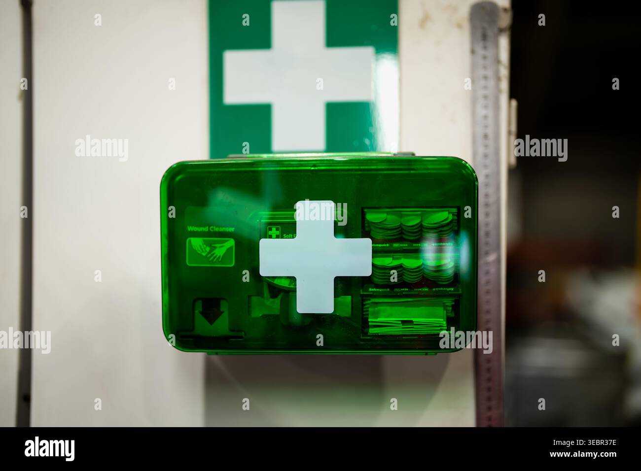 Grünes, an der Wand montiertes erste-Hilfe-Set mit weißem medizinischem Kreuz, sichtbarem Wundreiniger und Verbandsmaterial für die Einhaltung der Arbeitsplatzsicherheit in der Einrichtung Stockfoto