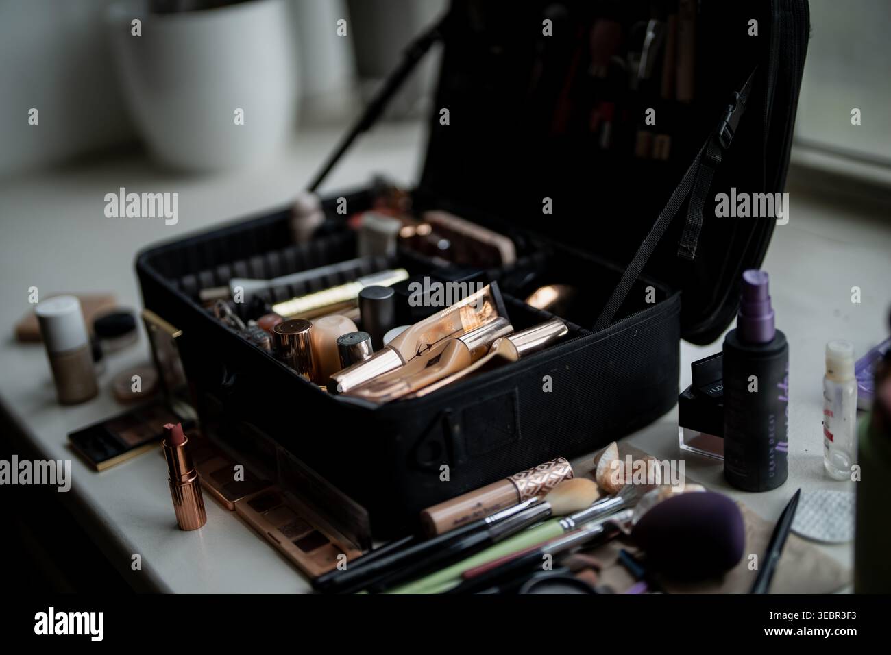 Schwarze Schminktasche gefüllt mit Bürsten, Kompakten, Paletten und Applikatoren neben Kosmetikprodukten für die Vorbereitung von Künstlern und den Kundenservice Stockfoto