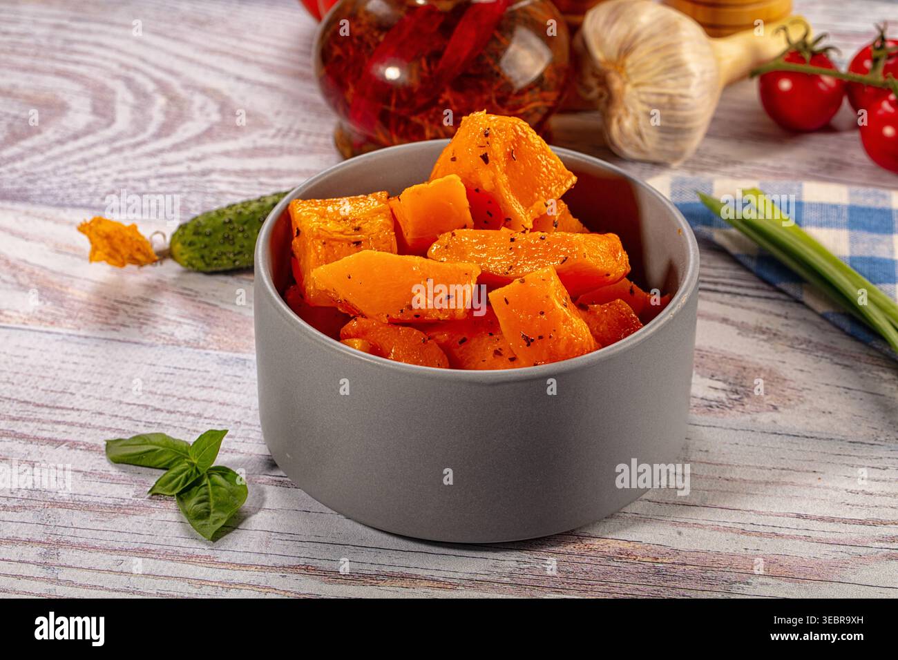 Gebackene, orangene Kürbisstücke, gewürzt mit Gewürzen in einer grauen Keramikschale. Gesundes vegetarisches Gericht auf hellem Holzhintergrund mit frischem Gemüse wie Bas Stockfoto